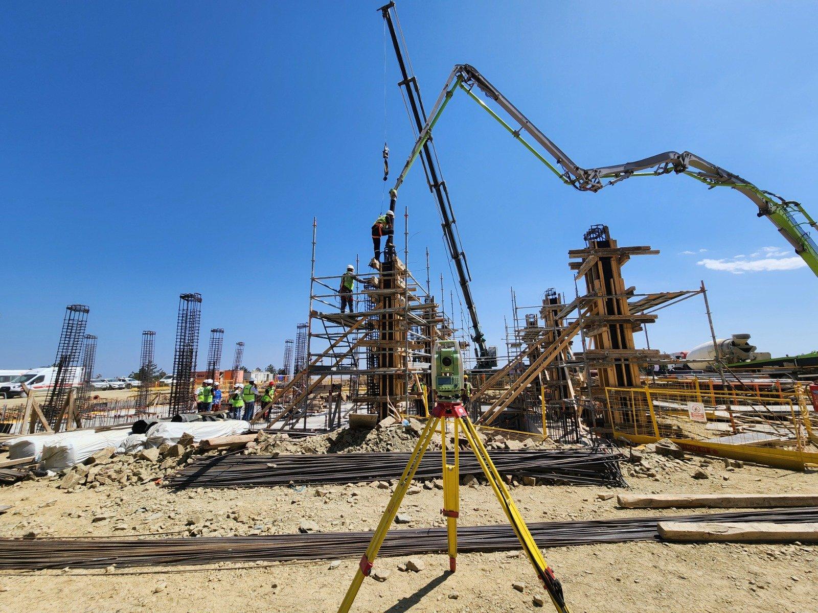 Şantiyede üçayak üzerindeki total station; arkada kalıp, donatı ve beton pompası